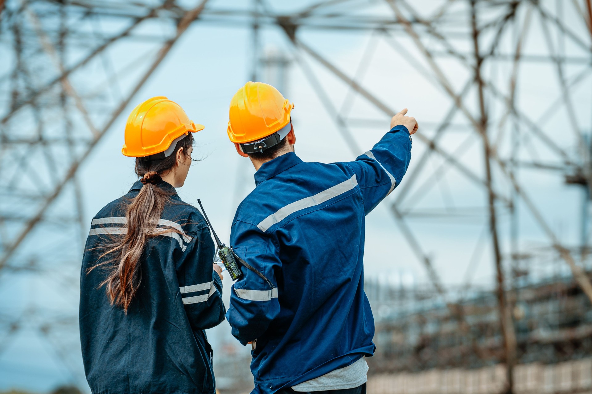 Engineers discussing project details at construction site with power lines and structures in the background